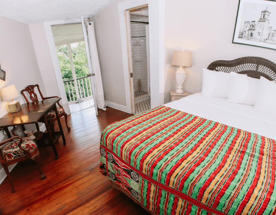 A cozy bedroom featuring a colorful quilt, a wooden table, and a door leading to a balcony.