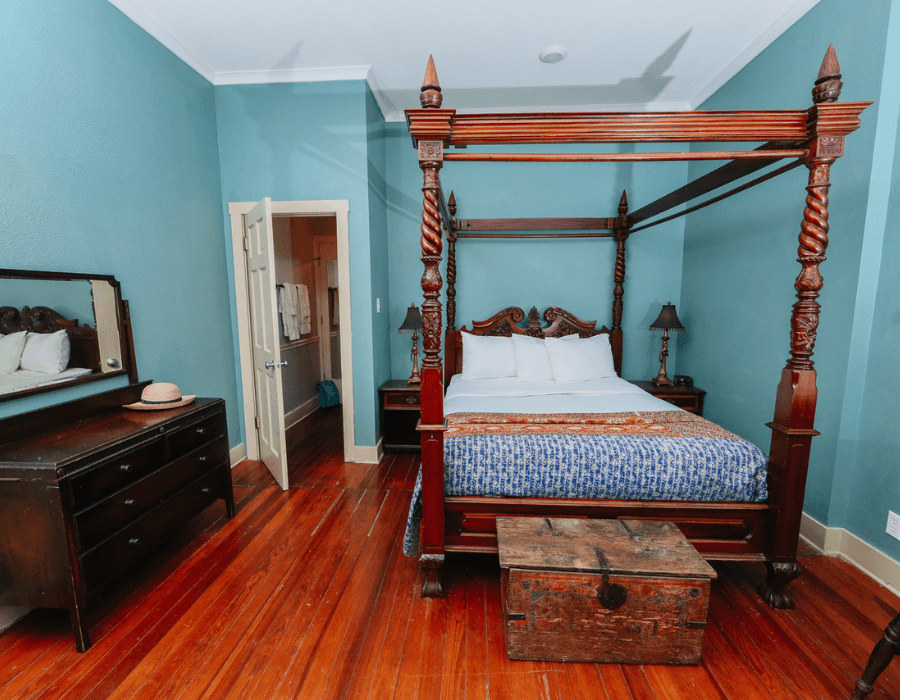 A warmly lit bedroom featuring a four-poster bed, wooden furniture, and blue walls.